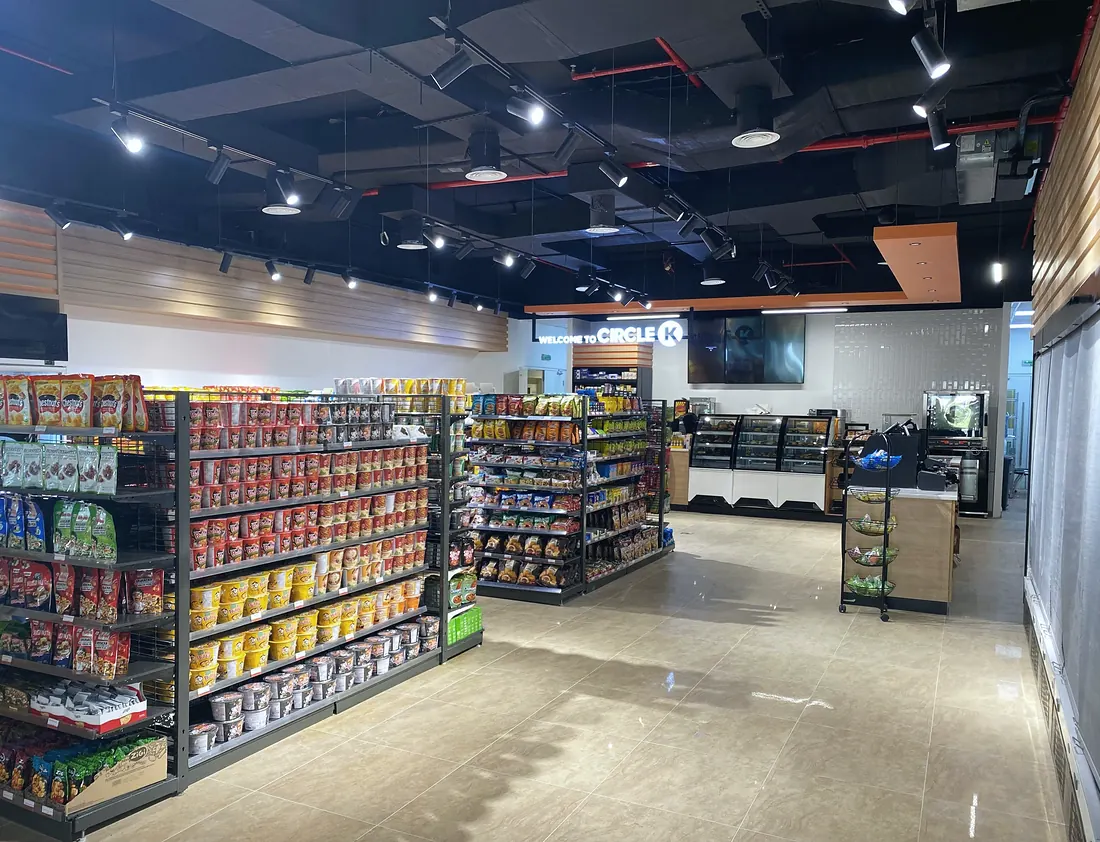 Circle K minimart, Al Ain: stocked aisles under an exposed black ceiling (frame 1 of 3)