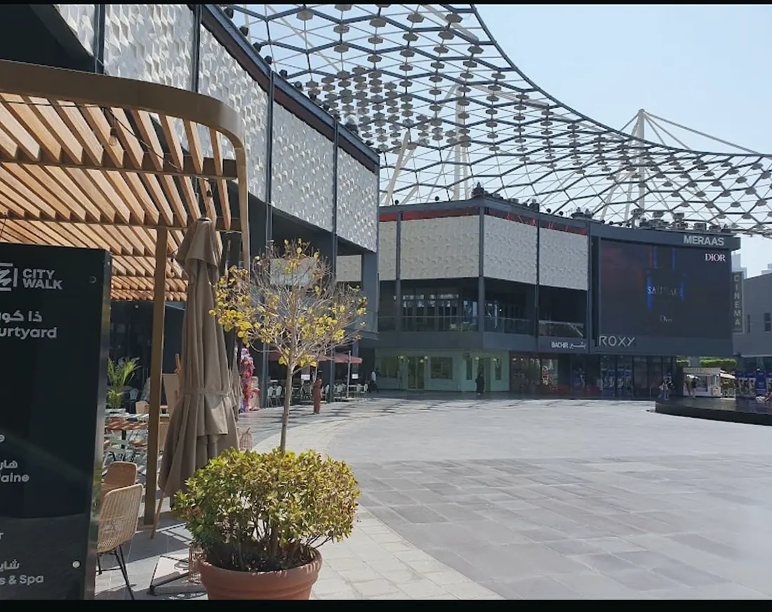 City Walk: paved courtyard and planters under the timber-ribbed canopy (frame 2 of 3)