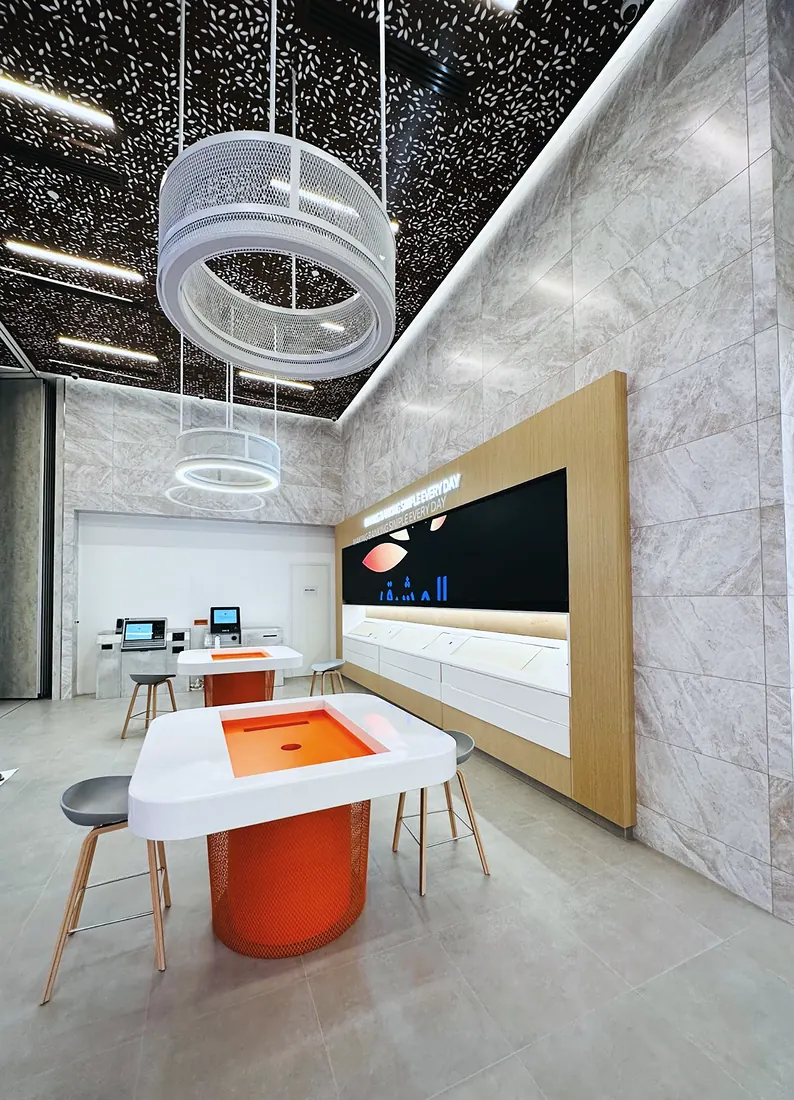 Mashreq Bank branch: ring pendant over an orange service pod, marble wall, perforated ceiling (frame 2 of 3)